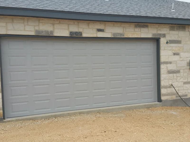 Gray garage door on a stone-clad house exterior in a rural setting.