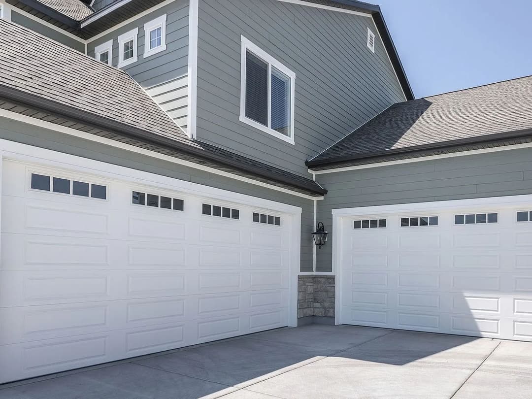 Modern home exterior with gray siding and double white garage doors. Bright sunny day.
