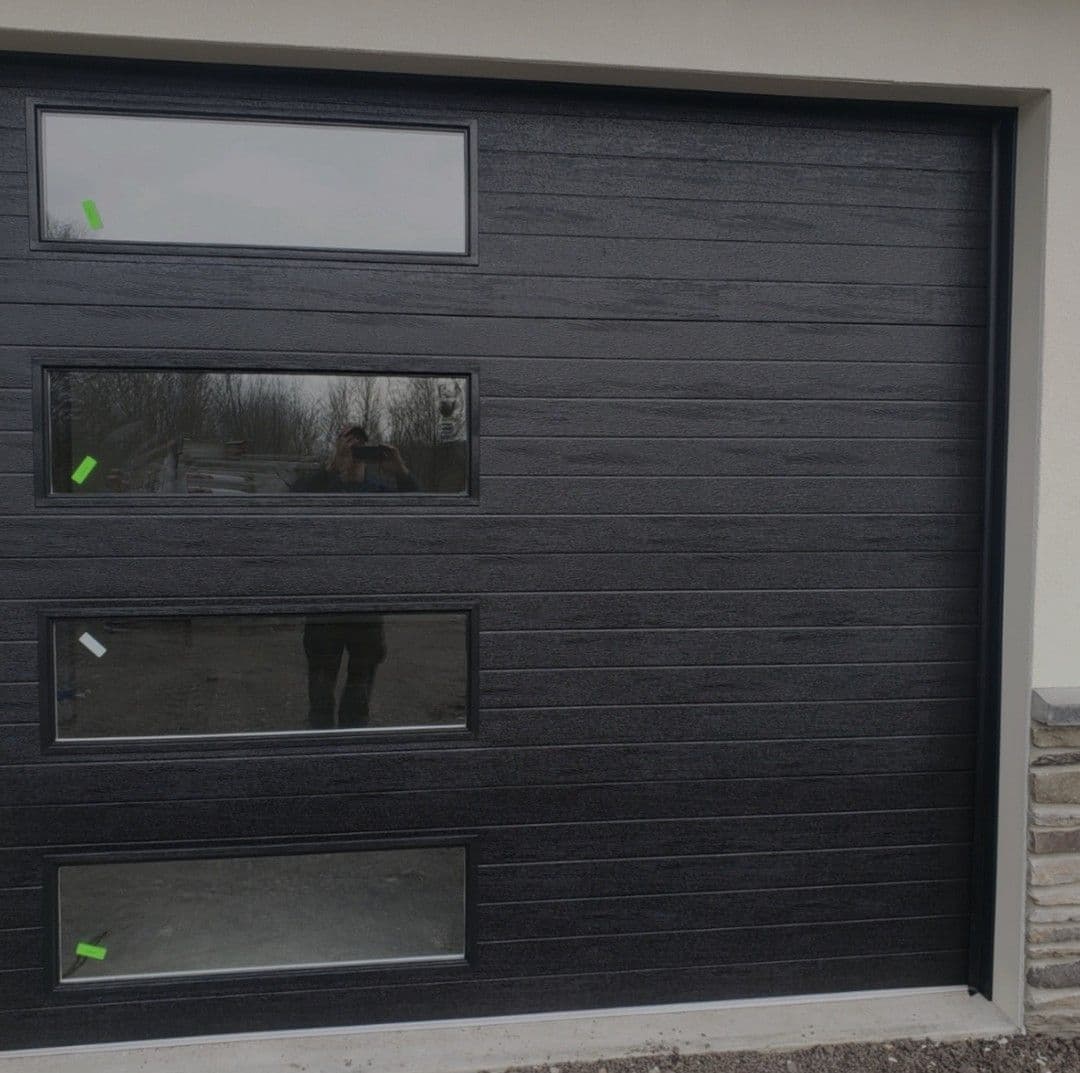 Modern black garage door with three windows, sleek design, and textured surface.