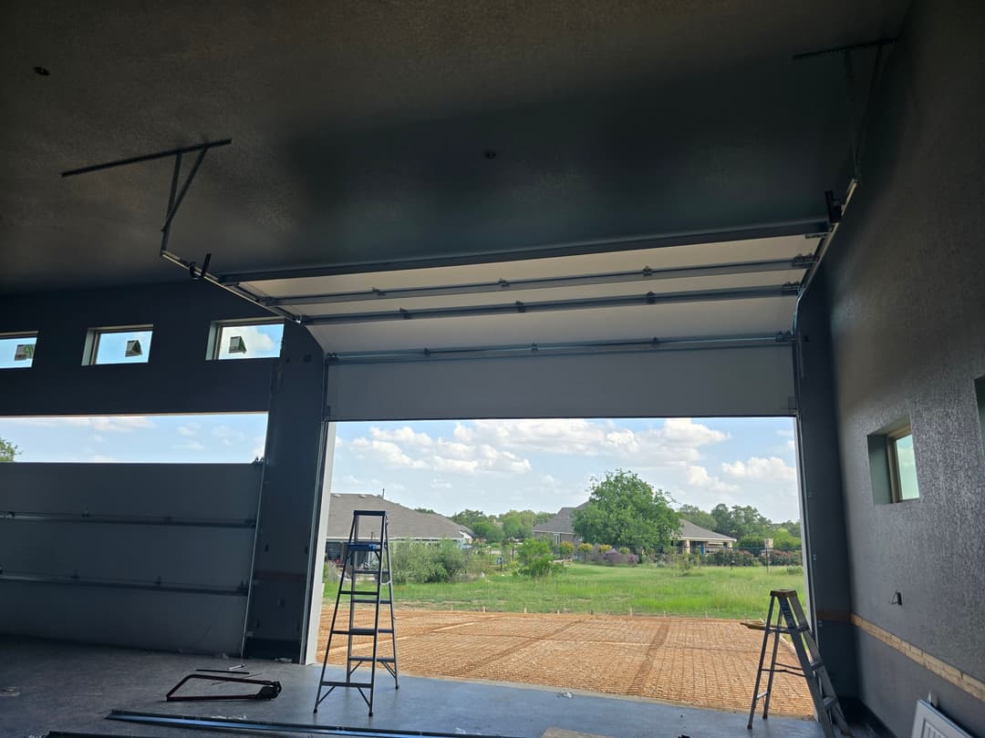 Interior view of a garage with open overhead door, showcasing a spacious outdoor area.