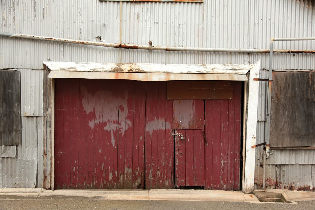 Weathered red barn door with rusty metal siding and faded paint, showcasing rustic charm.