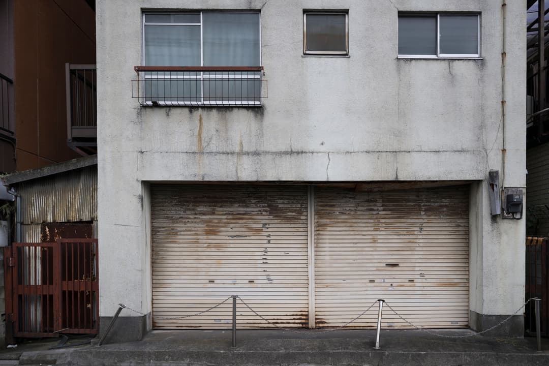 Abandoned building facade with rusted garage doors and windows in urban setting.