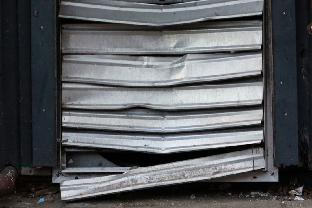 Grimy metal vent cover partially opened on urban sidewalk.