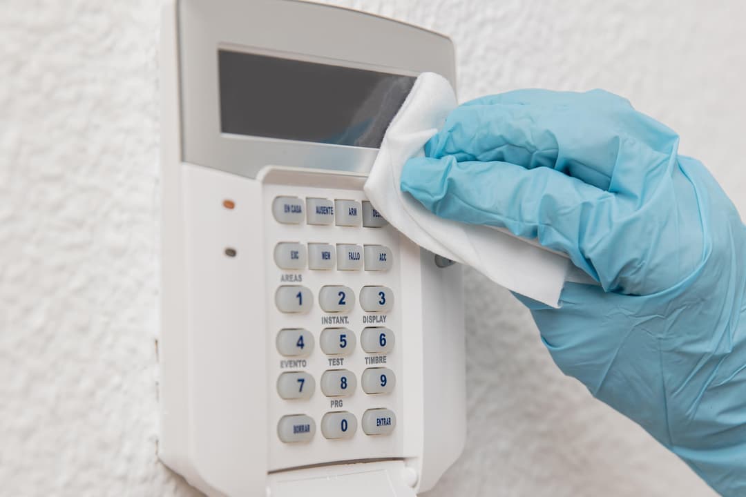 Person cleaning a wall-mounted security system keypad with a cloth.