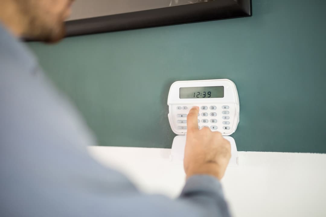 Person setting a digital alarm clock on a green wall, time displayed: 12:39.
