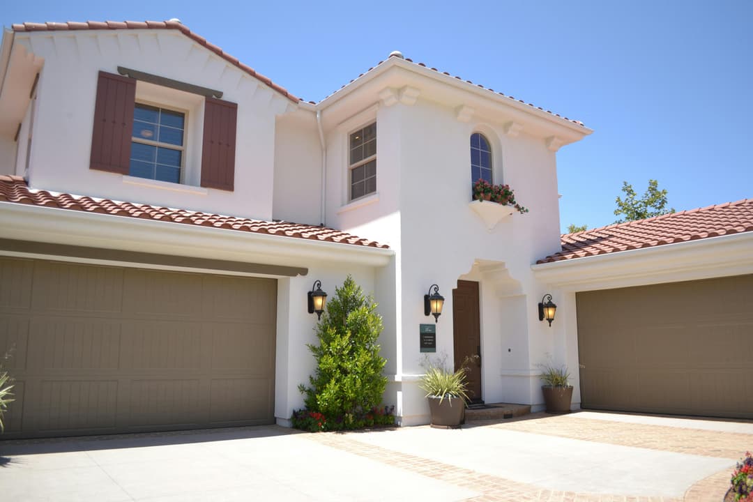 Modern white house with red tile roof, two garages, and landscaped entryway.