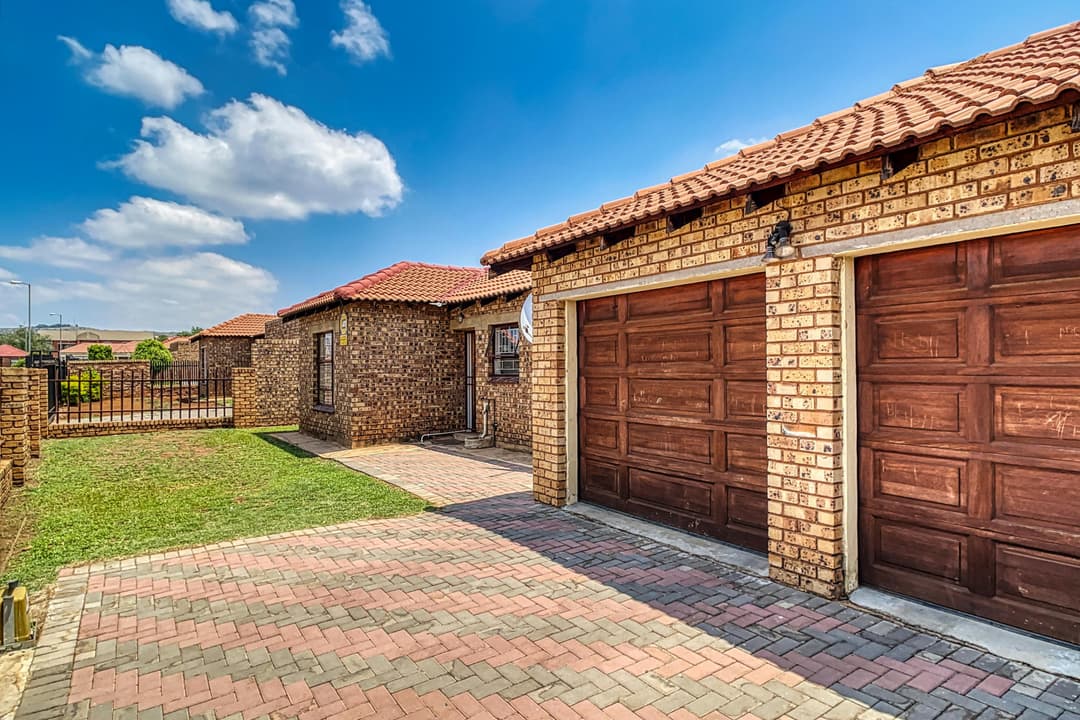 Modern brick home with red roof, two garages, and paved driveway under a clear blue sky.