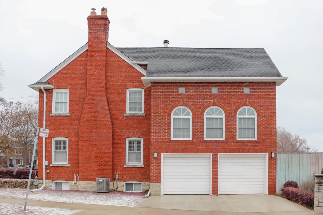 Red brick house with garage doors, three arched windows, and a chimney on a snowy street.