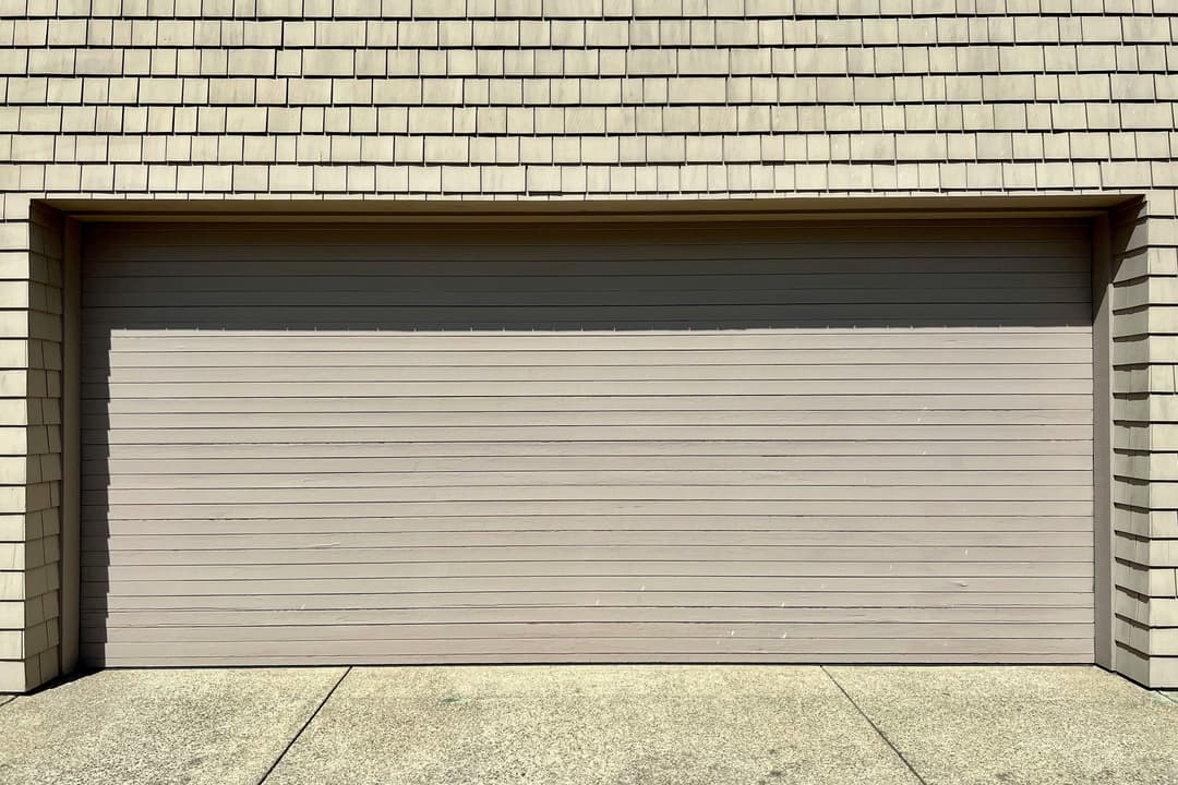 Wooden garage door with horizontal slats against a textured beige wall.