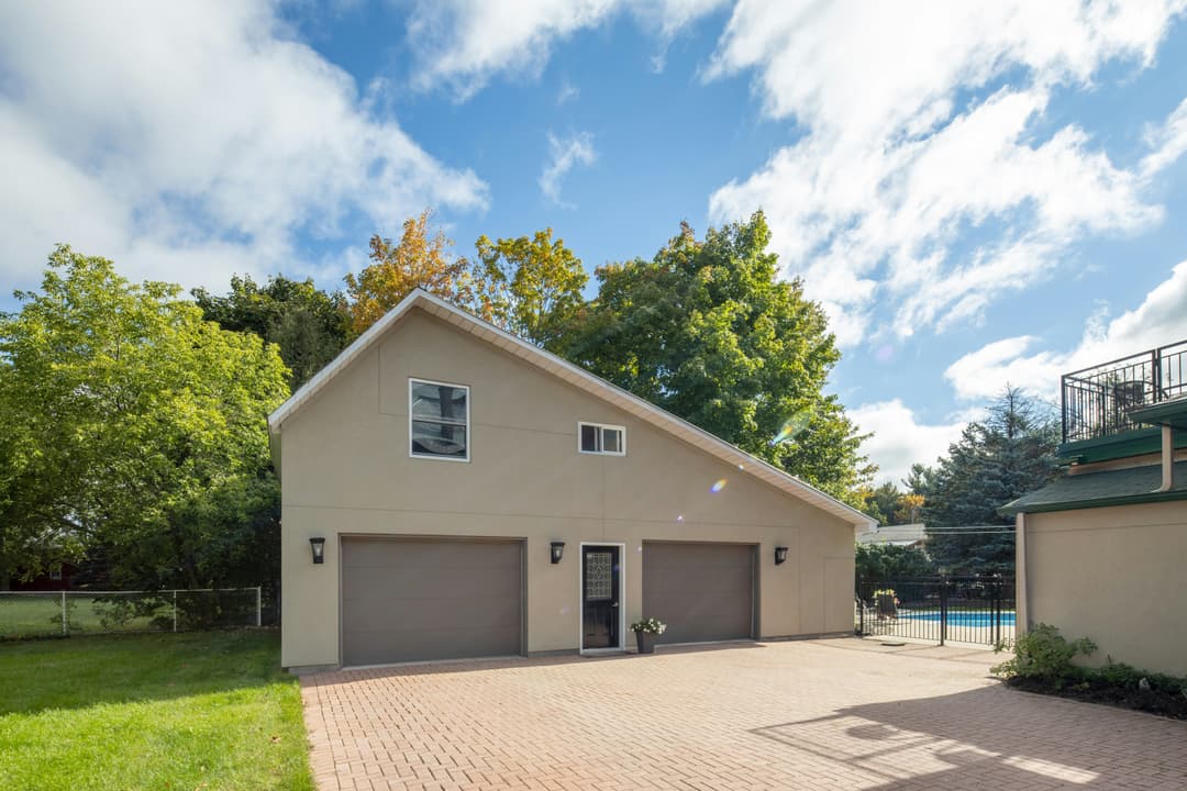 Two-car garage with brown doors, surrounded by greenery under a blue sky.