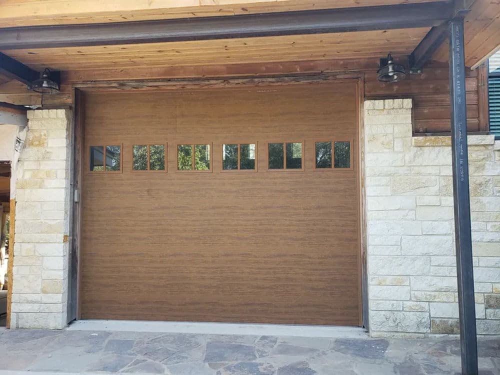 Wooden garage door with glass panels, set against a stone and wood exterior.