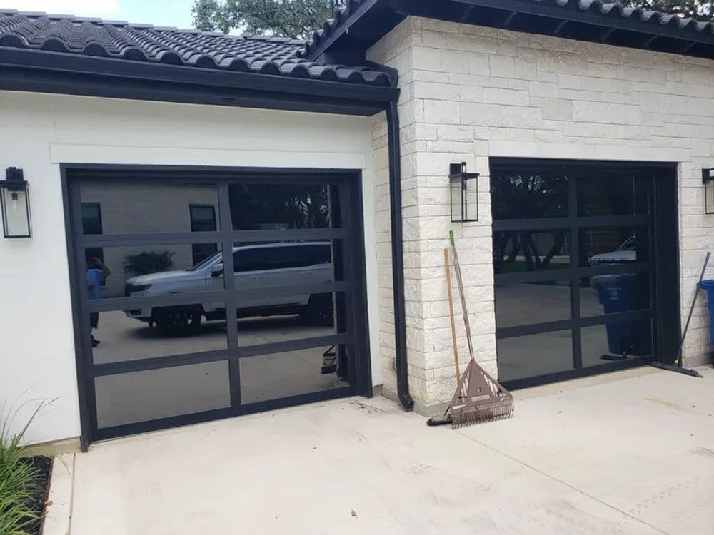 Modern garage doors with black frames and windows, adjacent to a contemporary stone home.