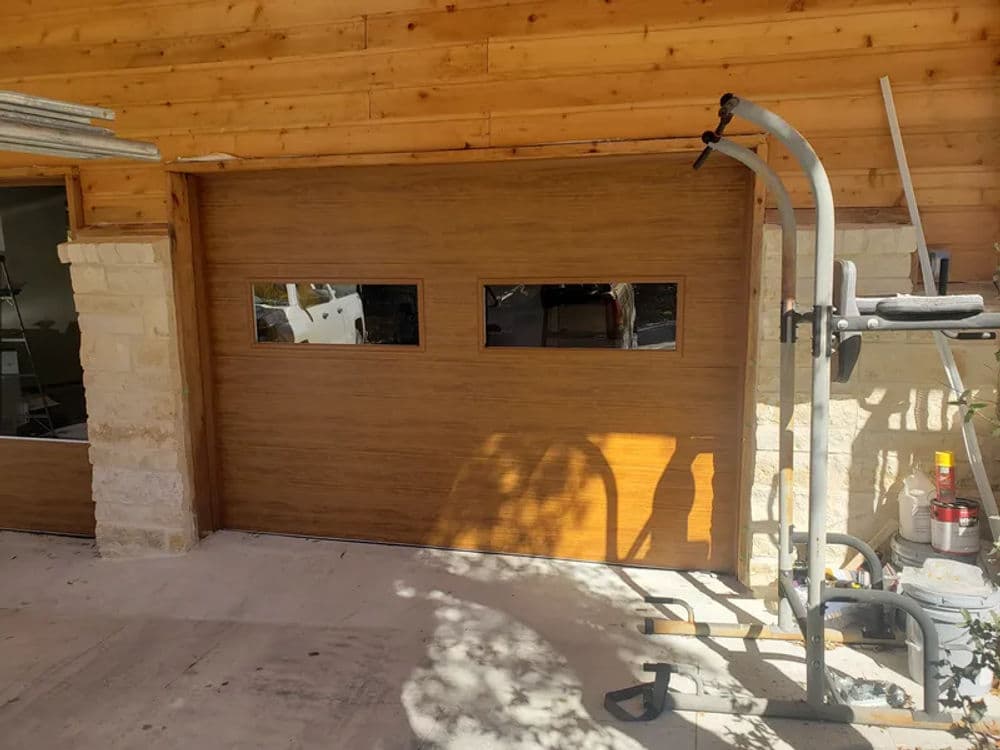 Modern wooden garage door with window panels next to exercise equipment.