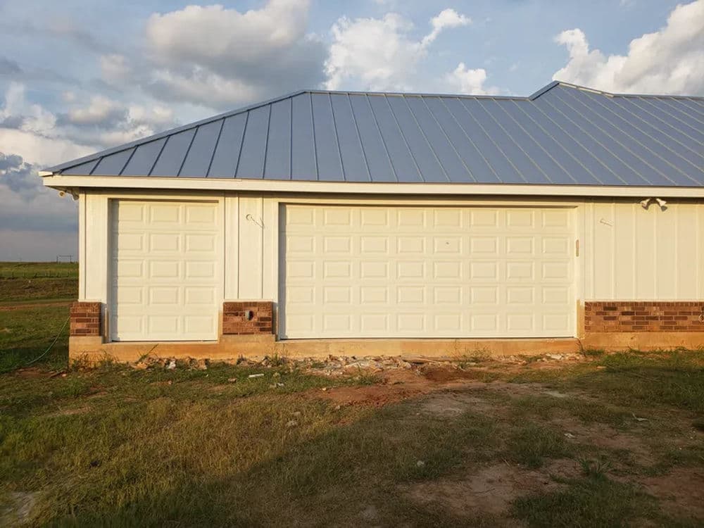 Modern two-car garage with white doors and a metal roof against a blue sky backdrop.