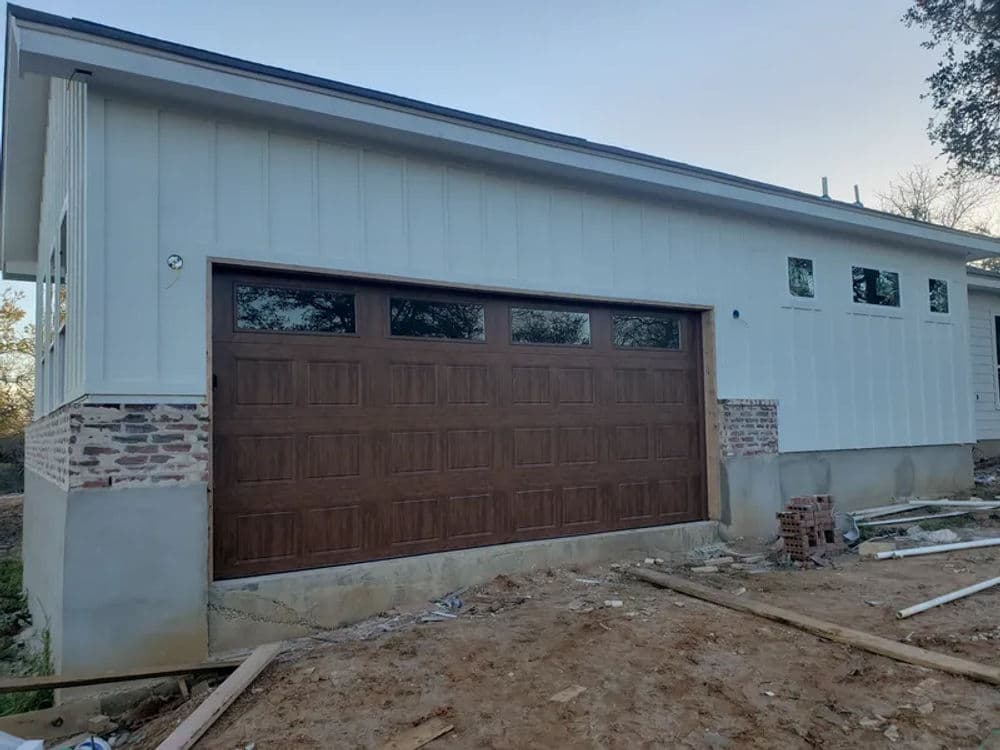 Modern house exterior with white siding, wooden garage door, and brick accents.